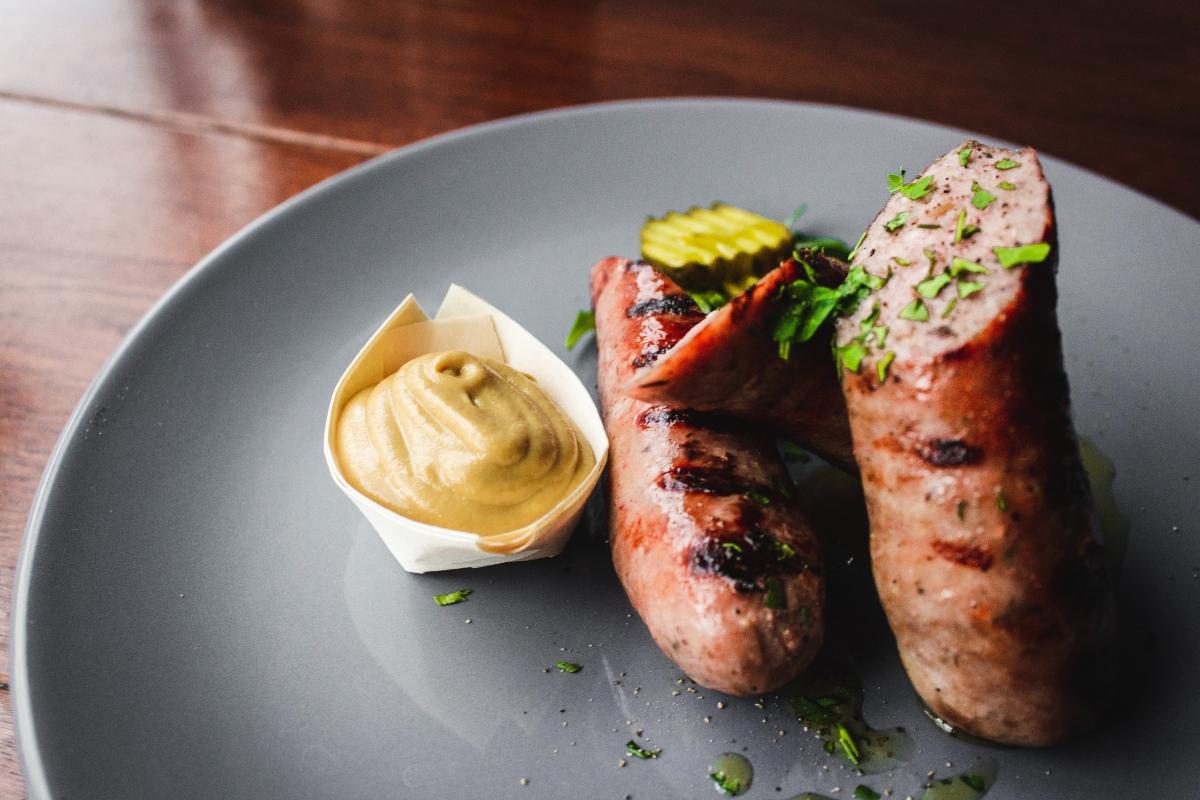 sausage on a plate with mustard and pickle