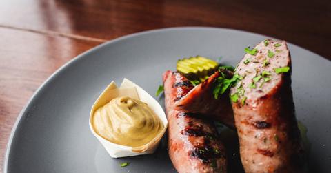 sausage on a plate with mustard and pickle
