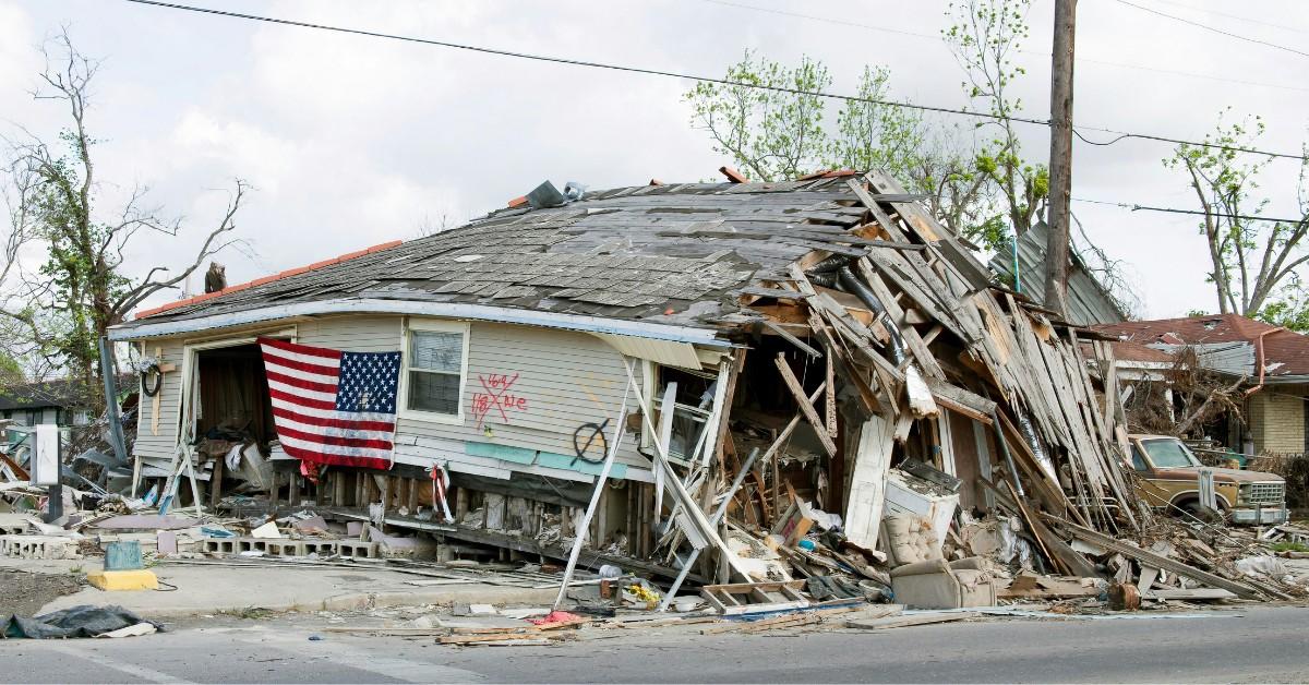 A home destroyed by storm damage hangs an American flag next to the rescue and recovery search markings