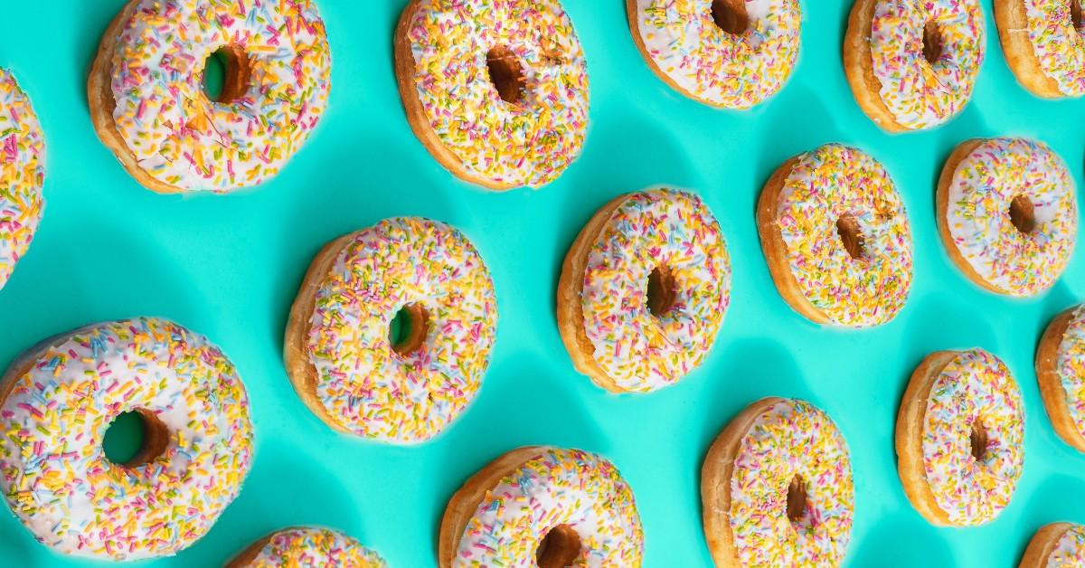 Frosted doughnuts covered in rainbow sprinkles are laid out against a blue background 