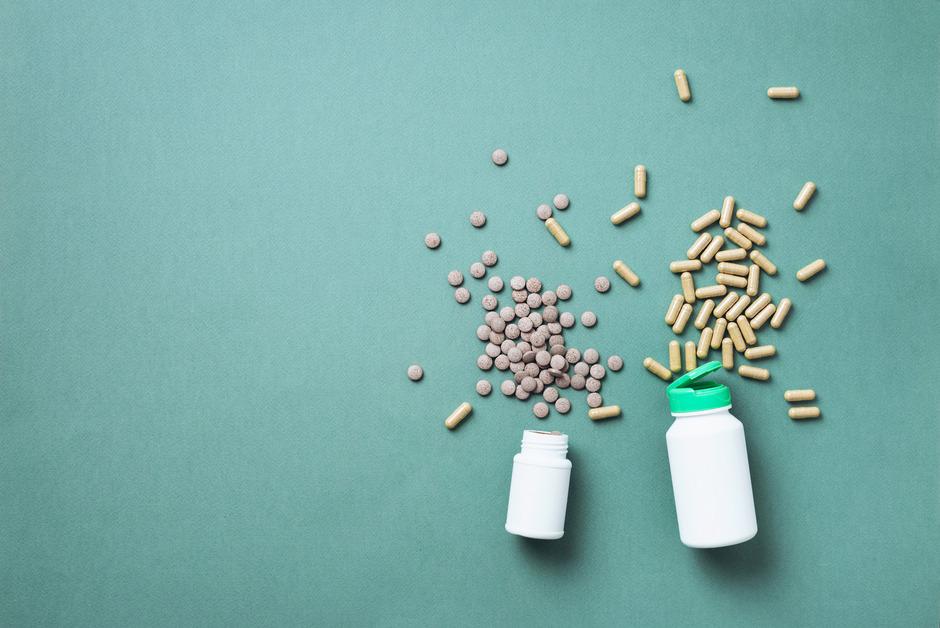 Two bottles of supplements spilled on a teal background. 