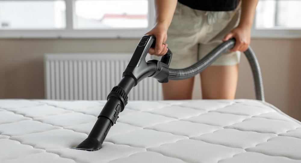 Someone is using a vacuum to clean a mattress. 