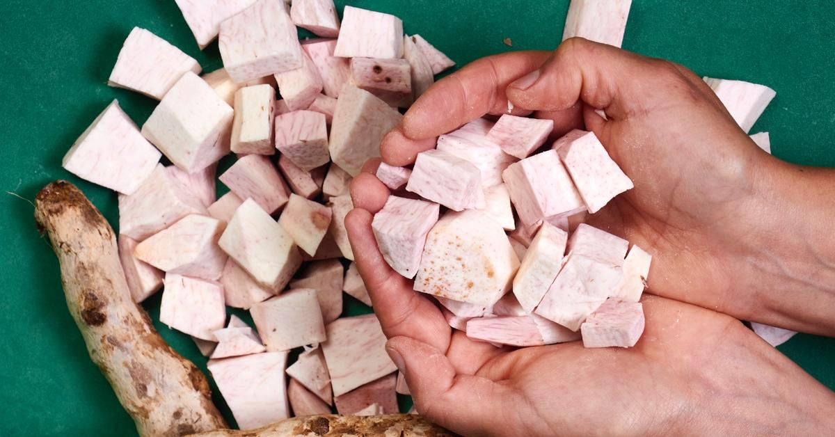 Person holding chopped pieces of taro root over a green work space. 