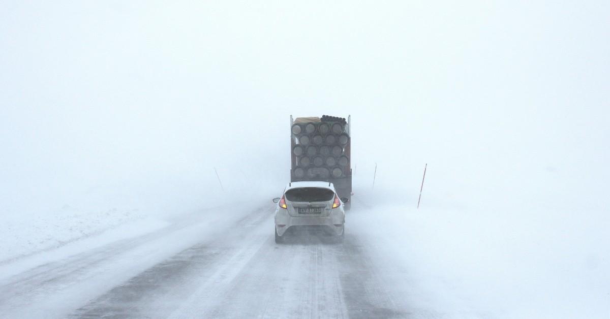 A car drives behind a big truck during a snow squall