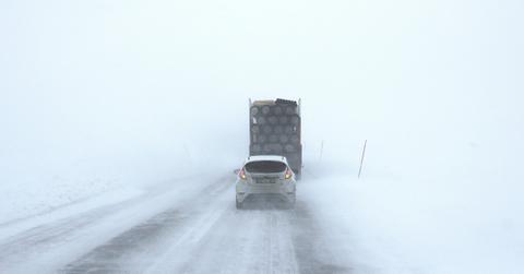 A car drives behind a big truck during a snow squall