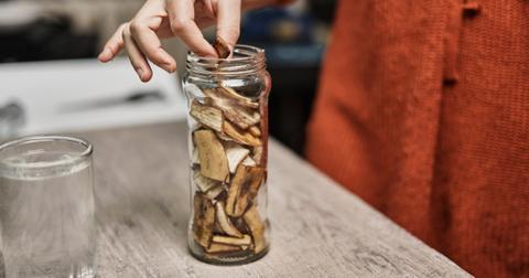 A person wearing a red sweater pulls a chopped banana peel piece from a glass jar.