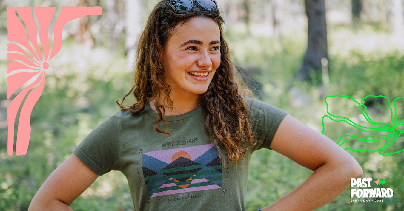 Taleah Hernández, wearing a green REI Co-op T-shirt and sunglasses on her head, smiles off to the side with her hands on her hips.