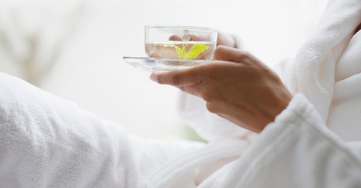 A person wearing a white robe, and holding a mug of tea.