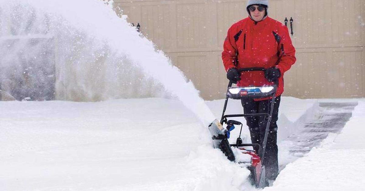 man in red jacket uses a snow blower in his garage.