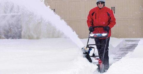 man in red jacket uses a snow blower in his garage.