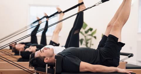 A row of people with their legs up using the bands of the reformer machine during a Pilates class.