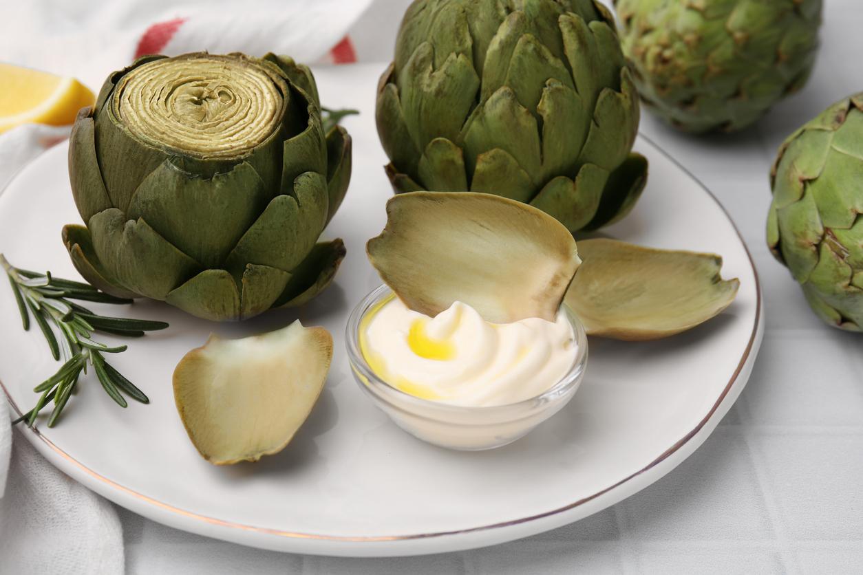 Artichokes are arranged artfully on a plate with a leaf dipped in a white cream condiment.