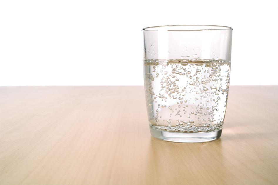 A small glass on a wood table containing sparkling water. 