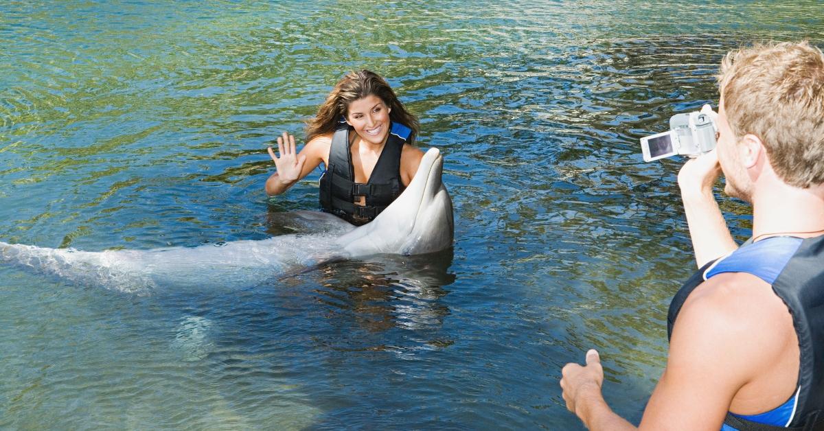 Man taking a video of a woman posing with a dolphin in water