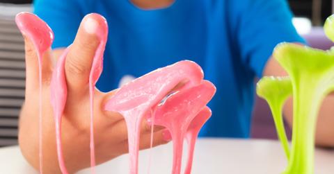A kid wearing a blue shirt shows hands covered in pink and green slime.