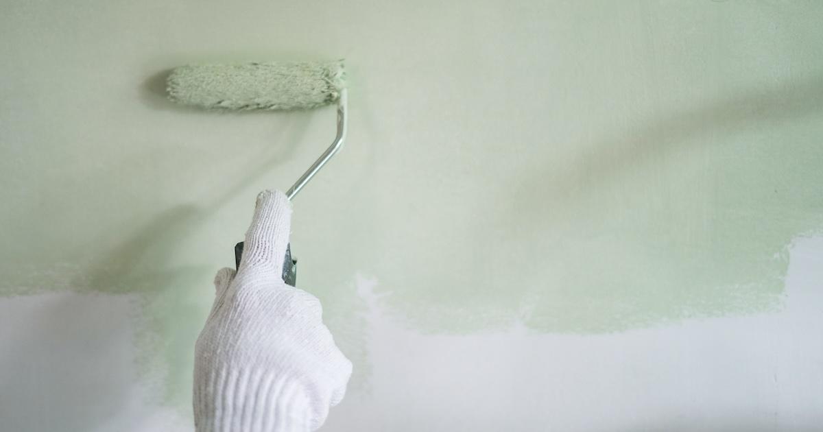 Hand holding a roller to paint a house light green