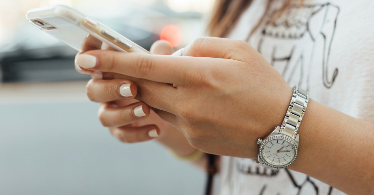 A woman with white fingernails holds her phone as she types