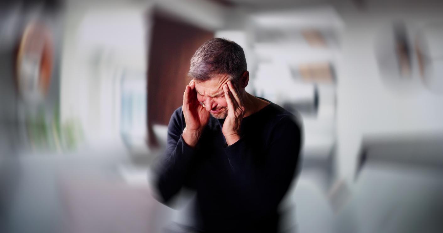 A picture depicts a man feeling dizzy with his hands on the temples of his head while the background is blurred and swirled.