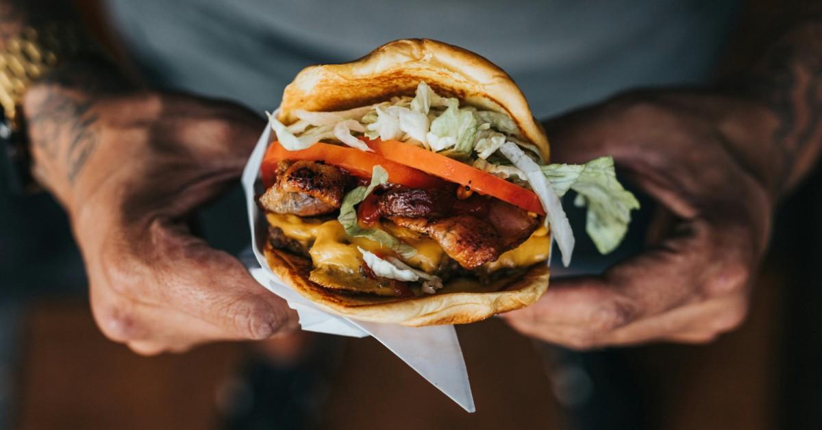 A pair of tattooed hands hold a hamburgers