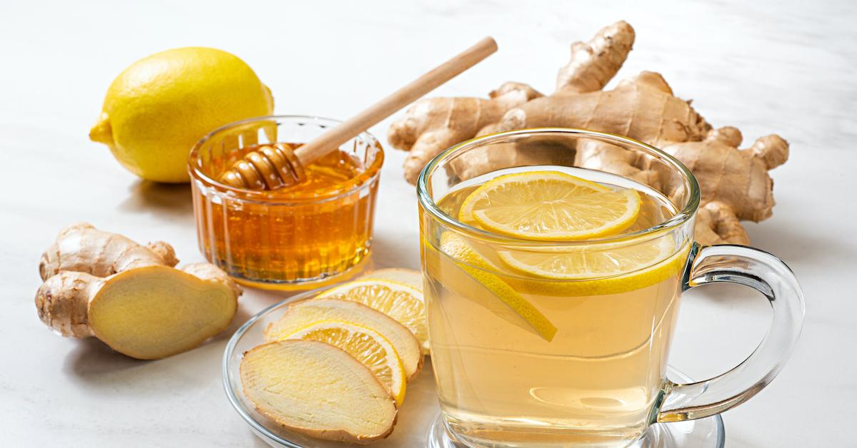 A stock image of tea with lemon, alongside slices of lemon, ginger, and a bowl of honey