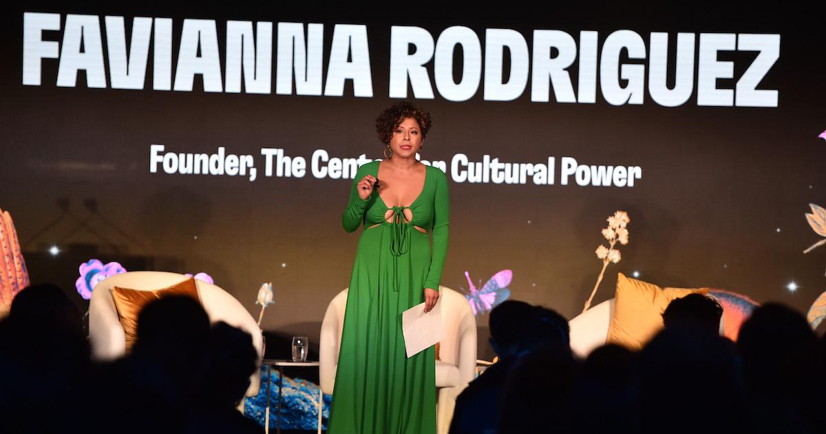 Favianna Rodriguez speaks onstage in a green dress.