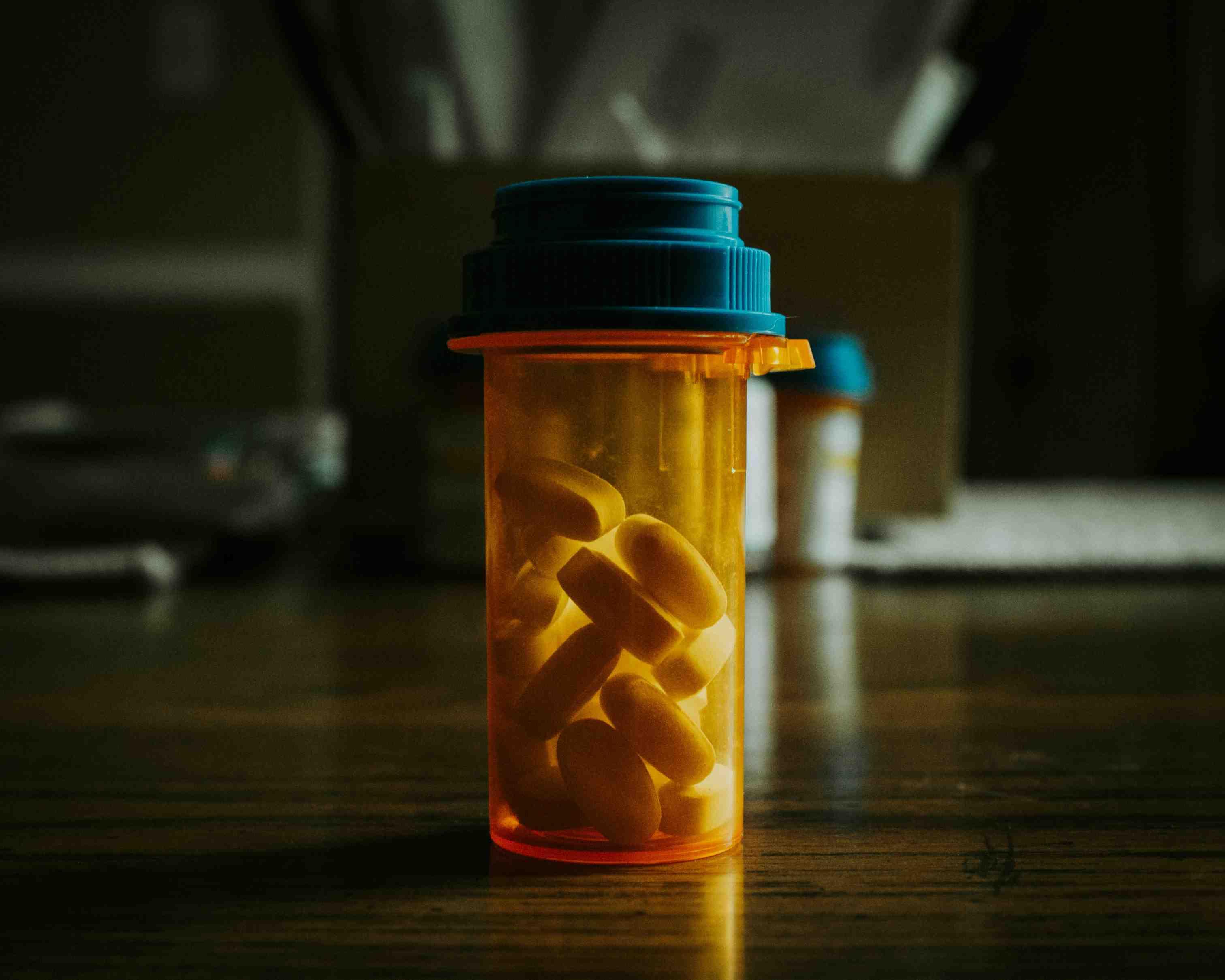 An unlabeled pill bottle is pictured with white pills inside it.