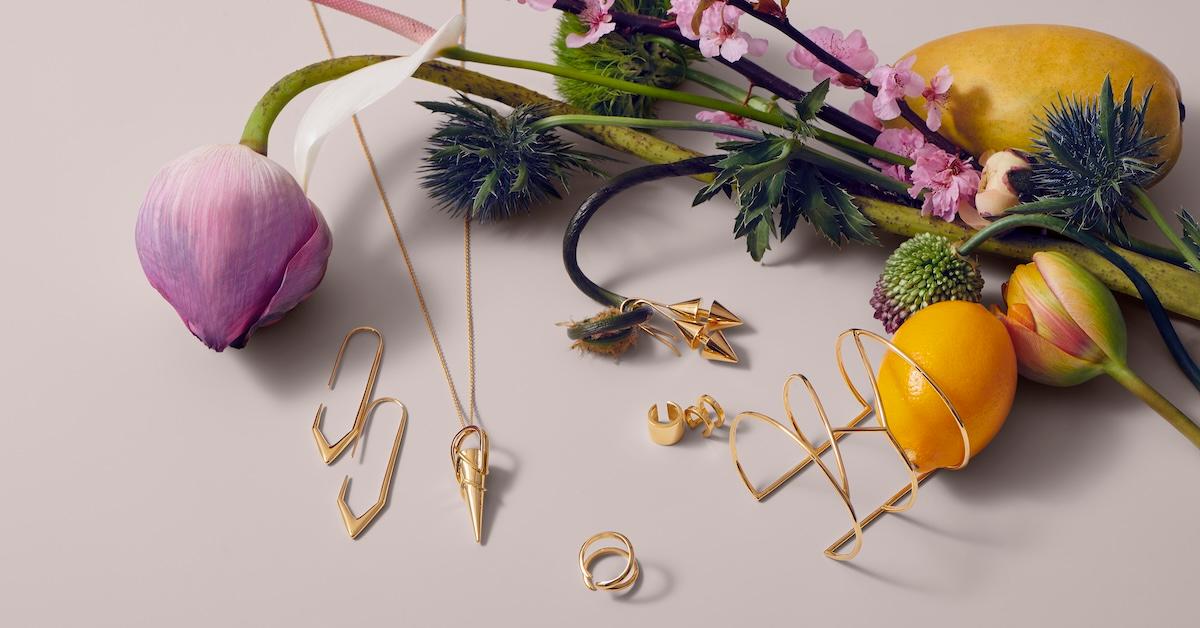 Flatlay of gold Auvere jewelry pieces alongside flowers and fruit.