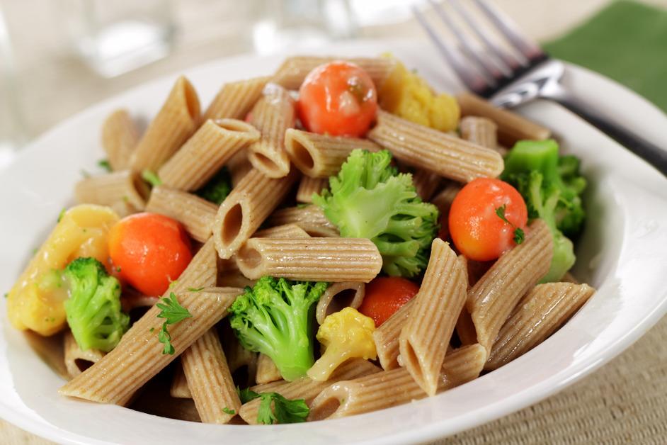 A close up photo of a bowl of whole wheat pasta with broccoli, tomatoes, and other vegetables. 