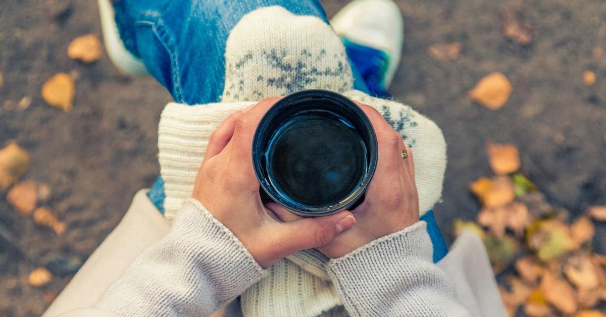 A woman holds her hot cup of coffee on a cool autumnal day