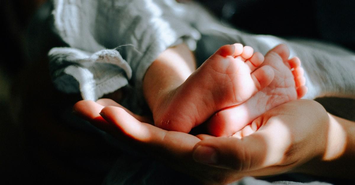 A mother holds her newborn babies feet up while the baby is snuggled up in a muslin blanket 