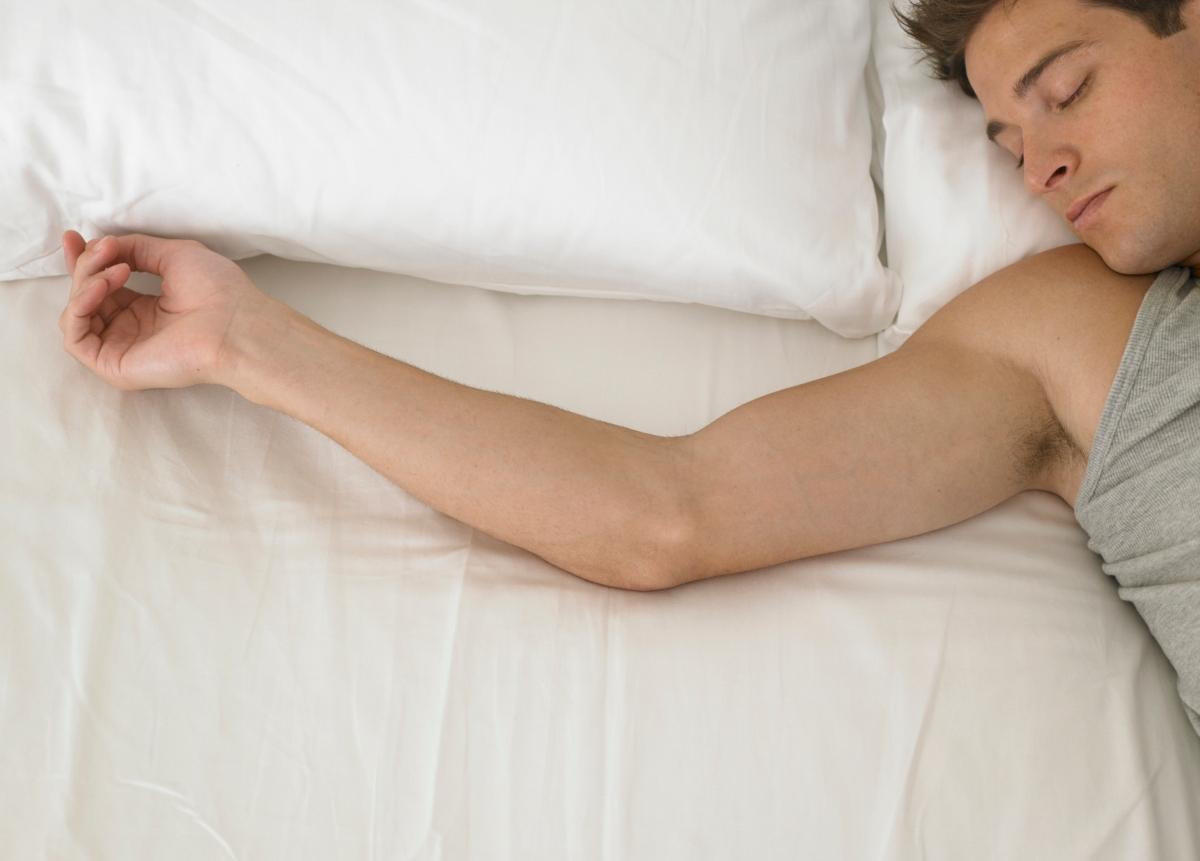 man sleeping with outstretched arm on white sheets