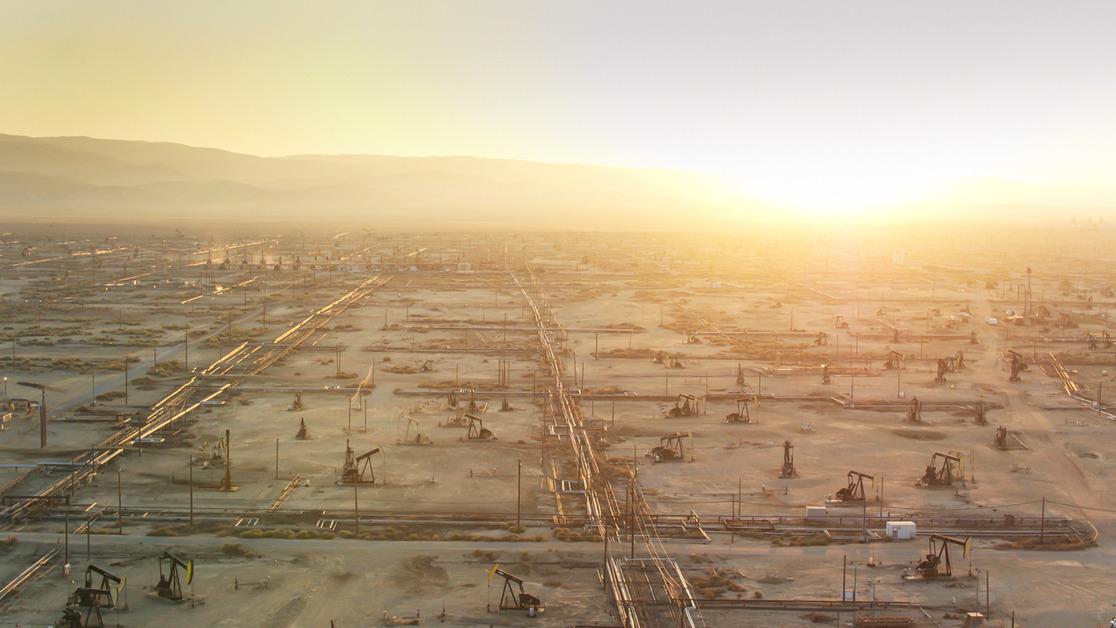 Photo of the sun setting behind the mountains near a large oil field. 