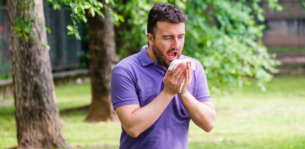 A man is sneezing into a tissue outdoors.