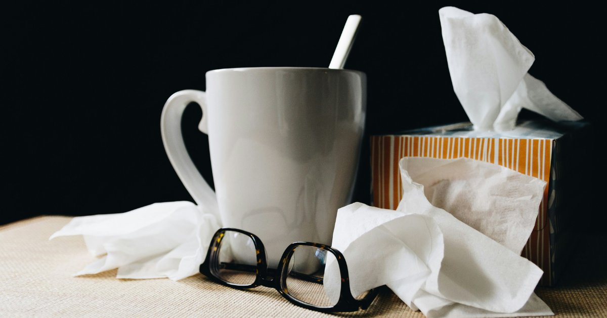 A cup of hot tea and pile of tissues sits on the nightstand of someone who is fighting a cold