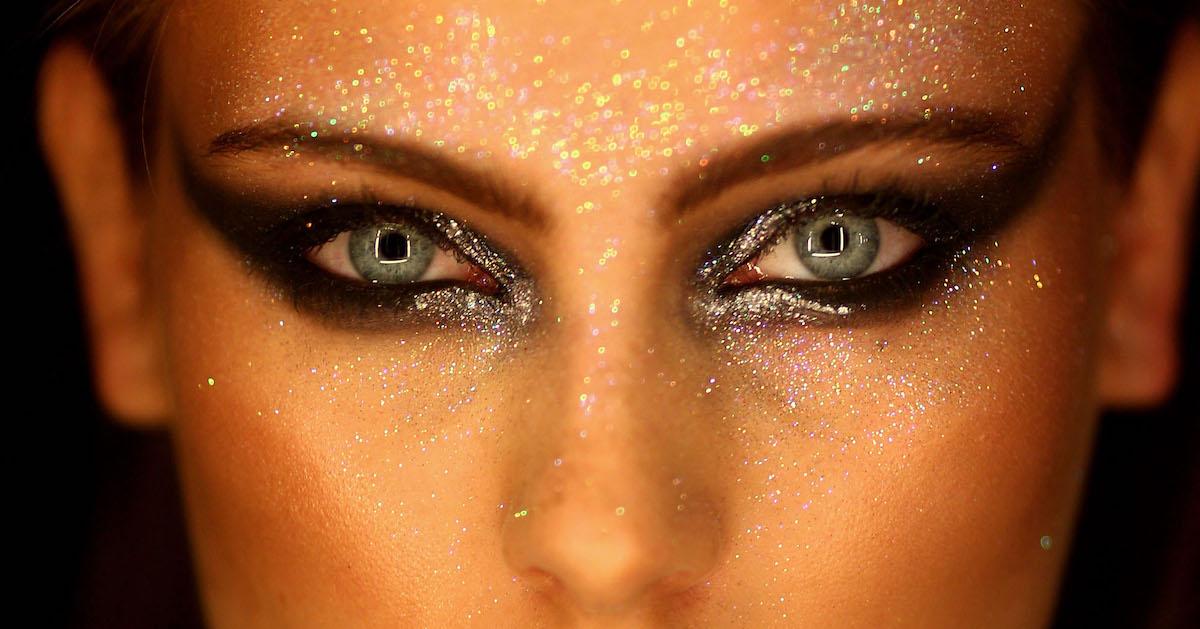 A closeup of a model's face with glitter and sharp black eye makeup.