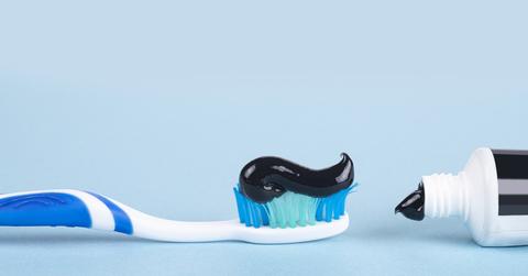 A close up photo of a toothbrush in line with a bottle of black toothpaste in front of a blue background.