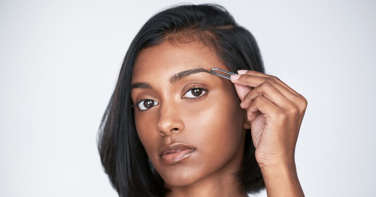 Southeast Asian woman carefully plucking the tail of her eyebrows. 