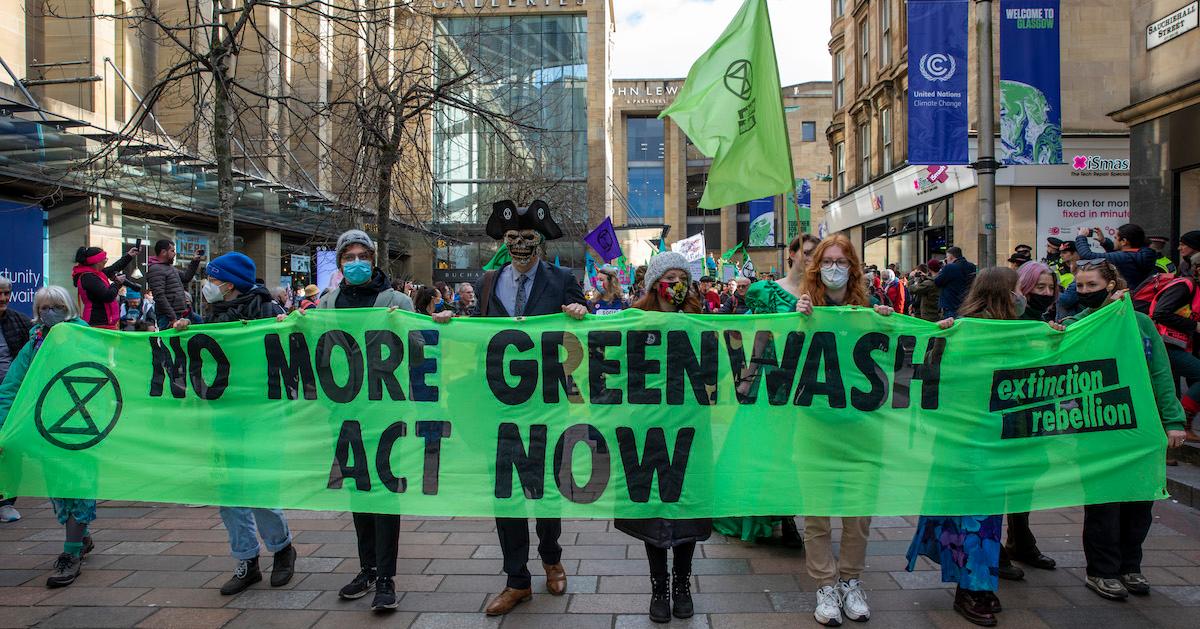 Activists in the street hold a green banner that reads "no more greenwash, act now" on Nov. 3, 2021 in Scotland, during COP26.