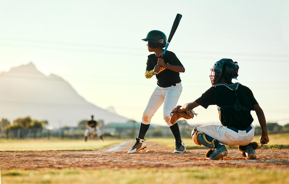 Two boys playing baseball with a mountain in the background during a sunny day. 