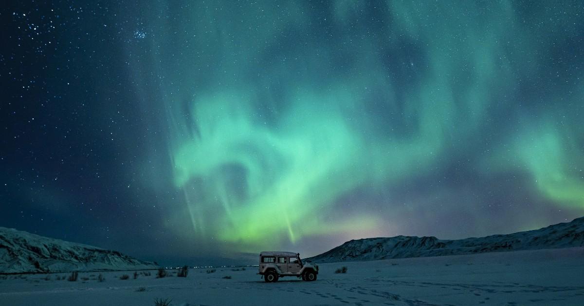 The northern lights swirl above a parked car