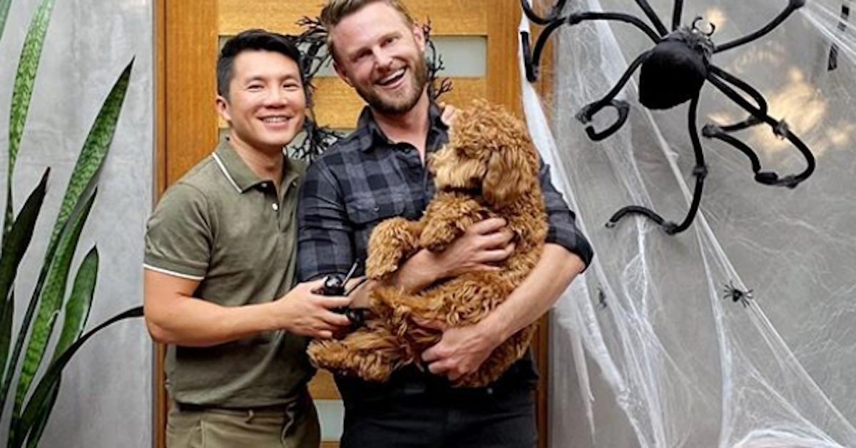 Bobby Berk and his partner smile and hold a dog.