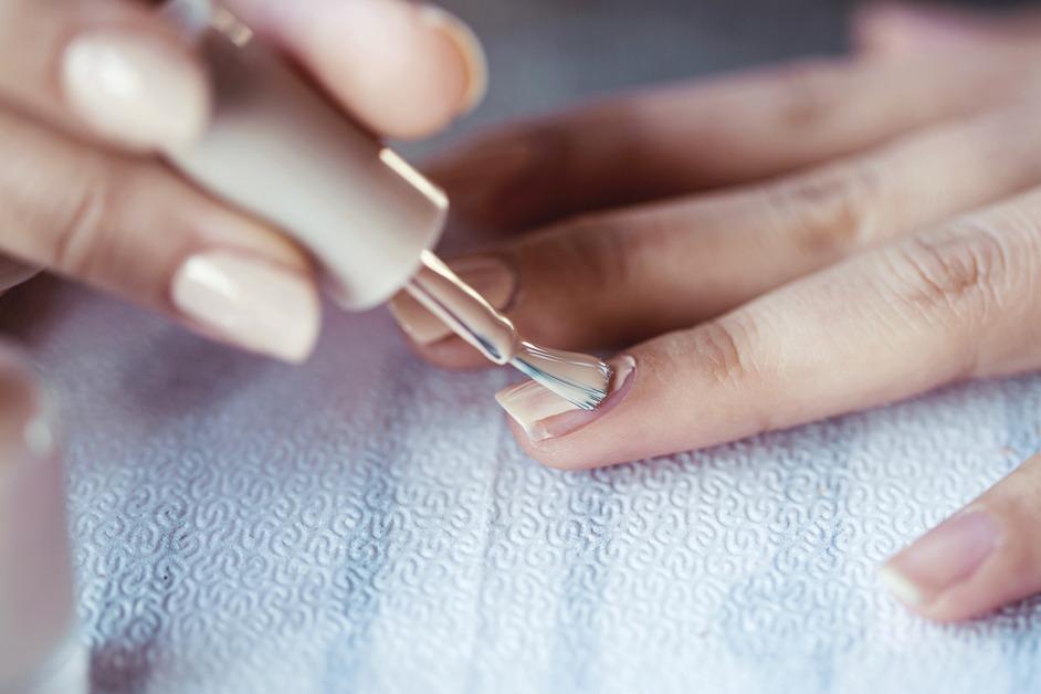 Manicurist applying nude nail polish to customer. 