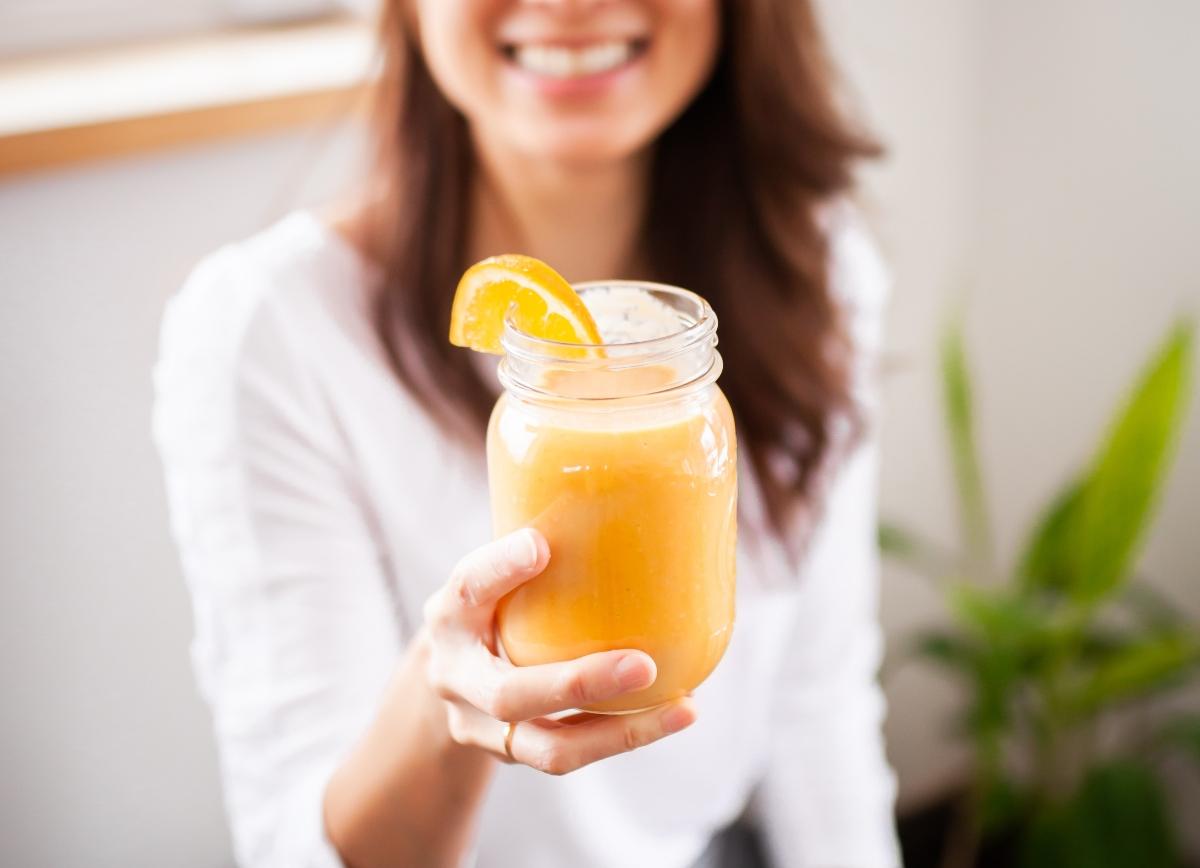 brunette holding orange smoothie with orange slice on edge