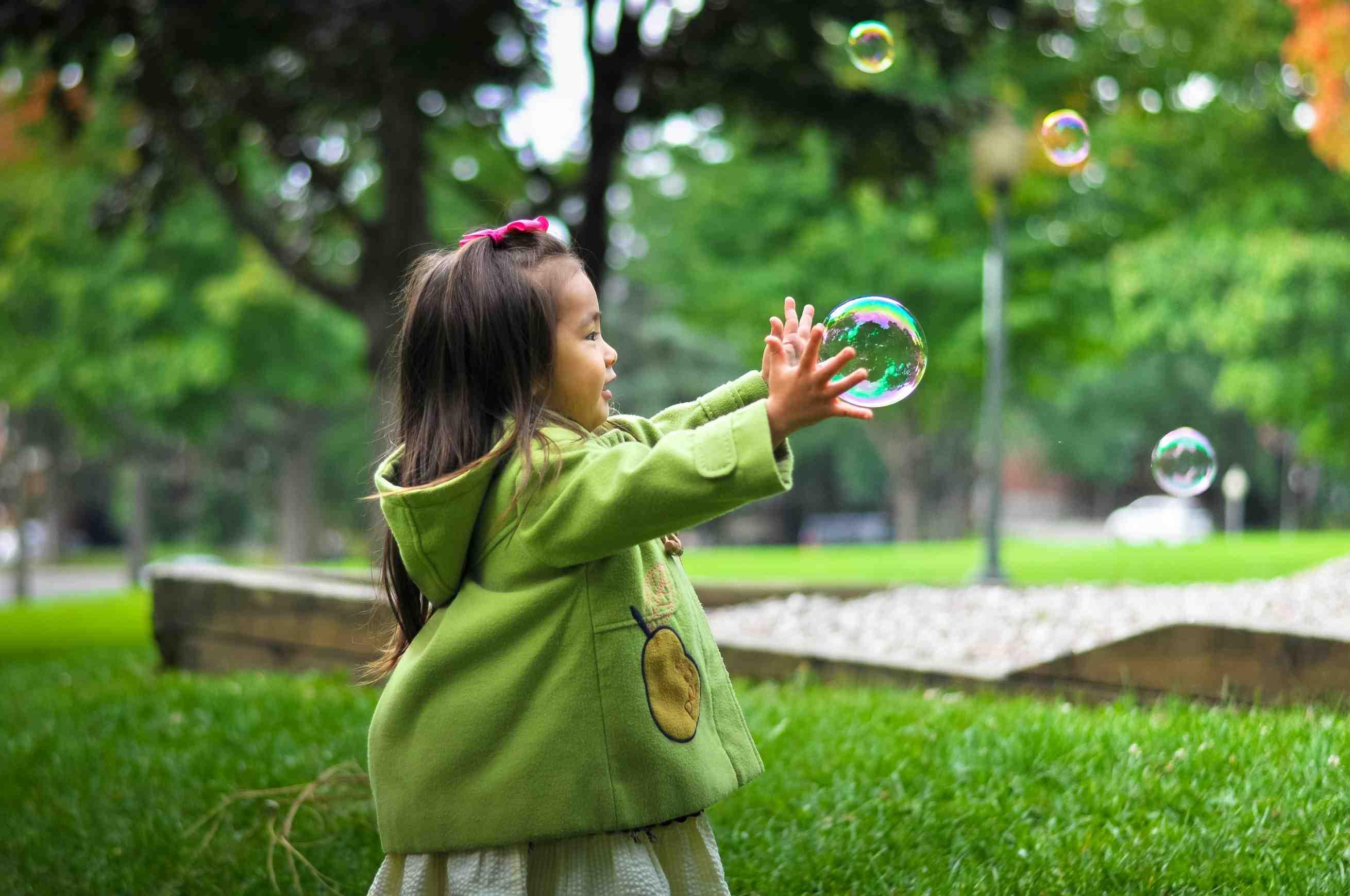 A young child plays with bubbles in the park.