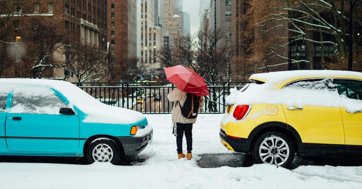 A person cuts between a blue car and a yellow car while navigating a snowy city street