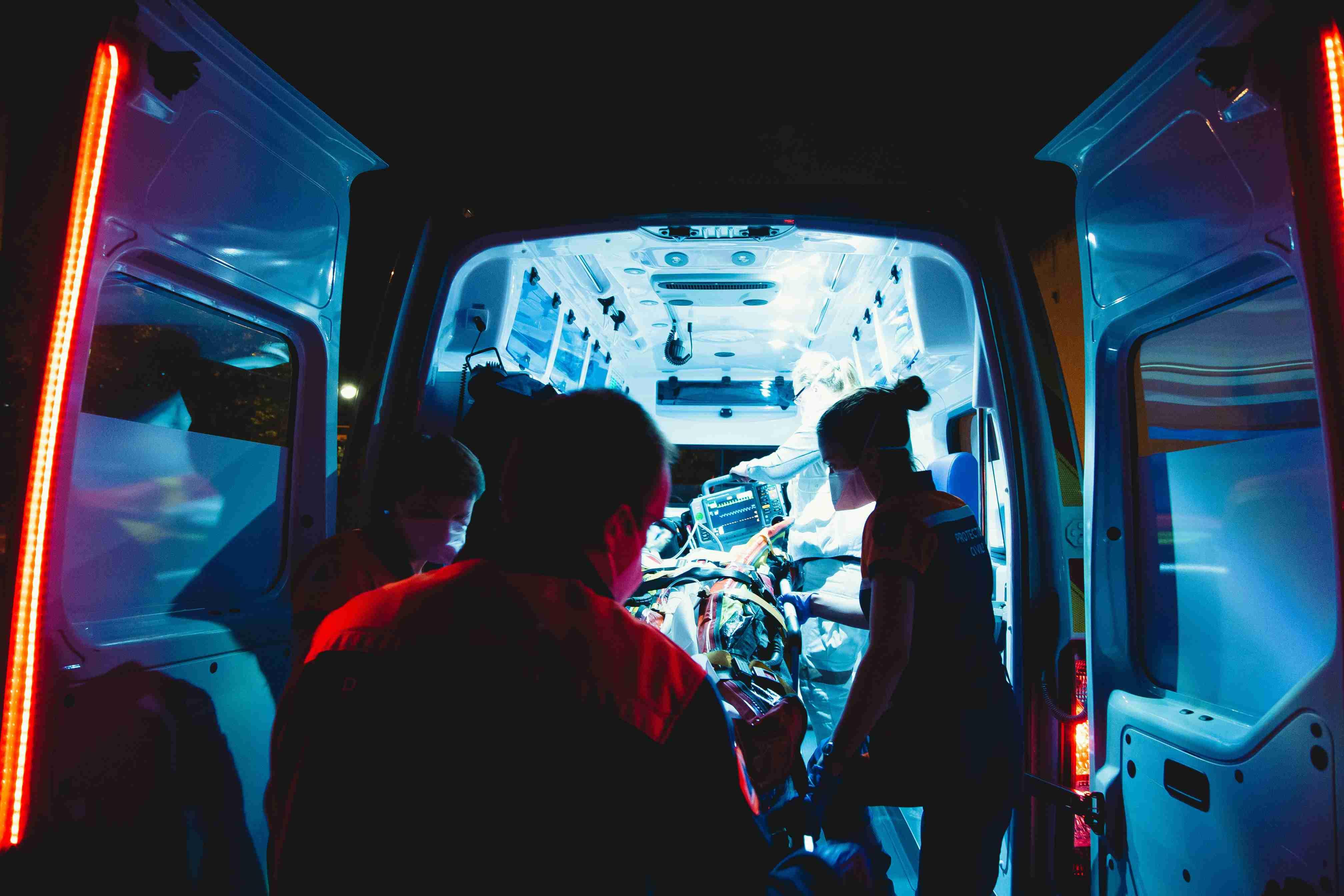 Emergency responders assist a patient into an ambulance at night.