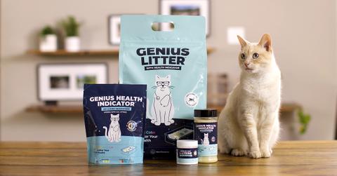 Photo of four Genius Litter products on a wooden surface beside a sandy-hued cat
