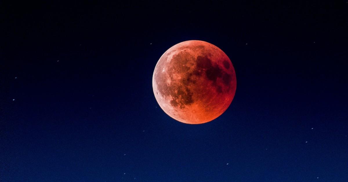 A slightly pink blood moon hangs in a star filled sky