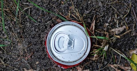An overhead view of a beer can in the dirt outside.