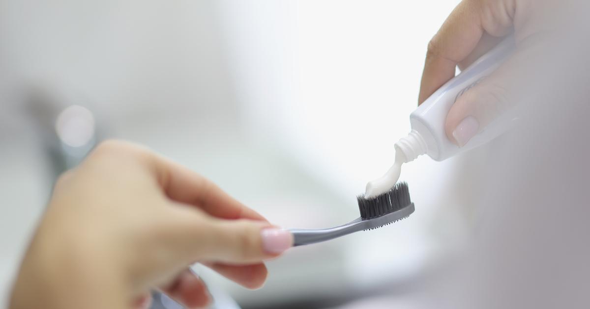 A closeup of someone applying toothpaste to a toothbrush.